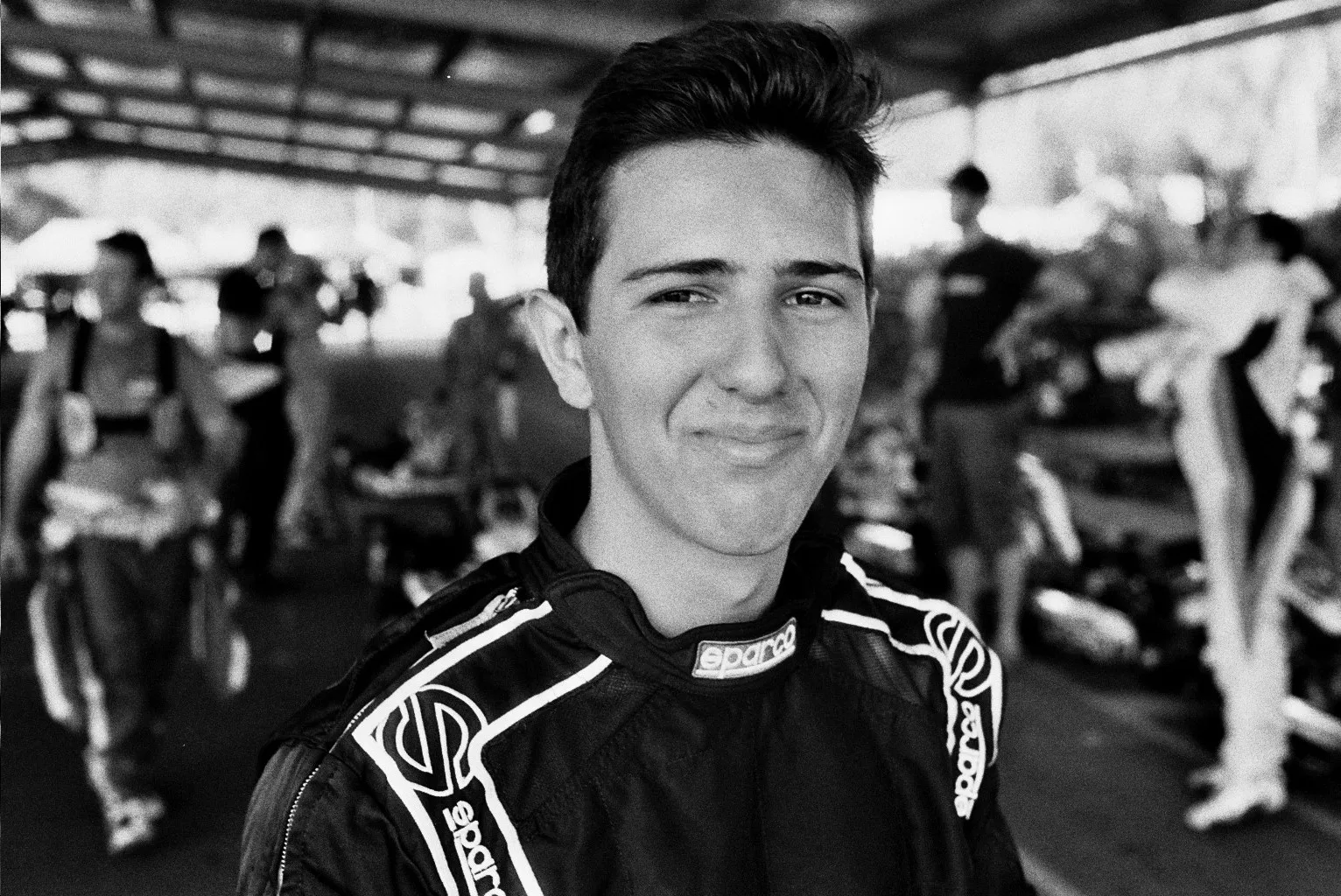 A portrait of a young man in a motor racing uniform.